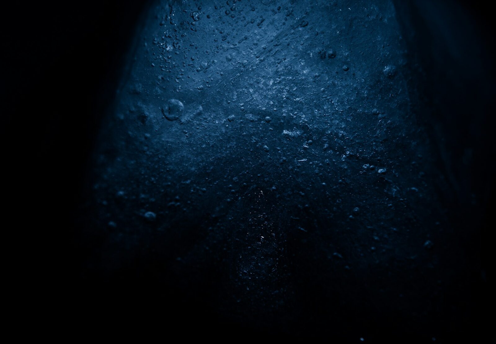 Clear ice against a deep blue background — macro close-up of cold water droplets forming on a frozen surface.