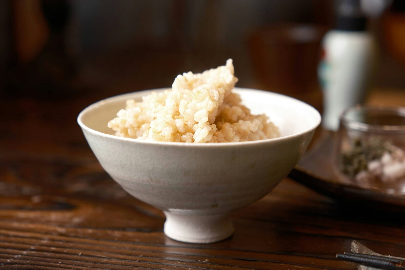 A white ceramic bowl filled with rice sitting on a wooden table — simple, traditional composition.